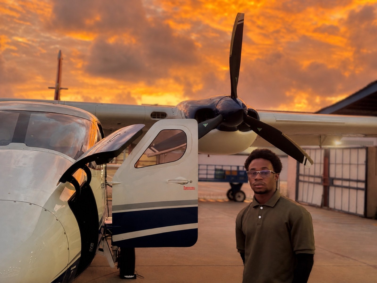 Michael A. Thom beside a Cessna aircraft under a fiery sunset, Guyana