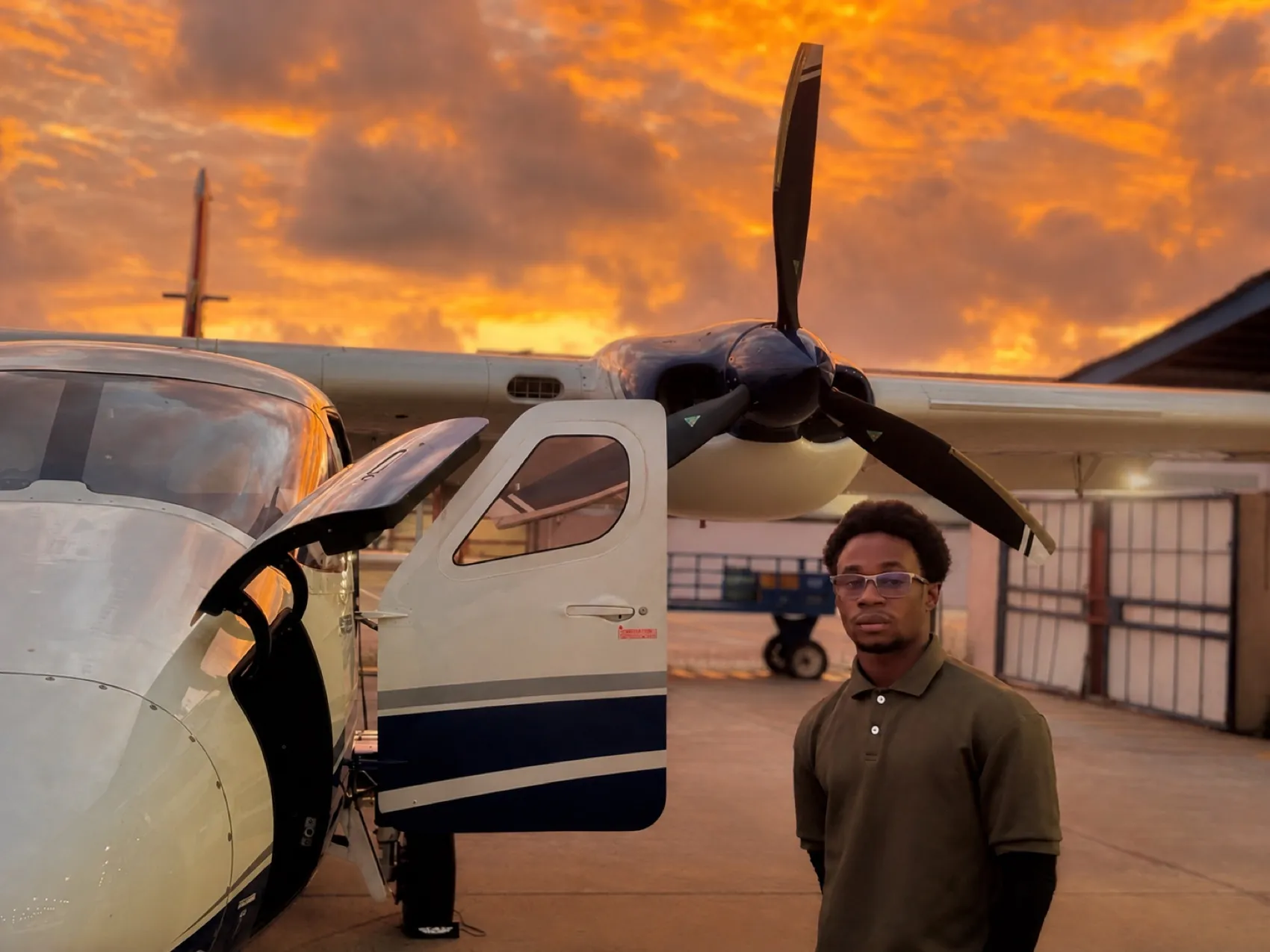 Michael A. Thom beside a Cessna aircraft under a fiery sunset, Guyana