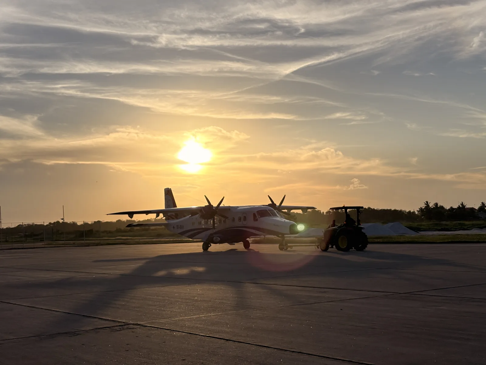 Twin-engine aircraft being towed across the apron at sunset